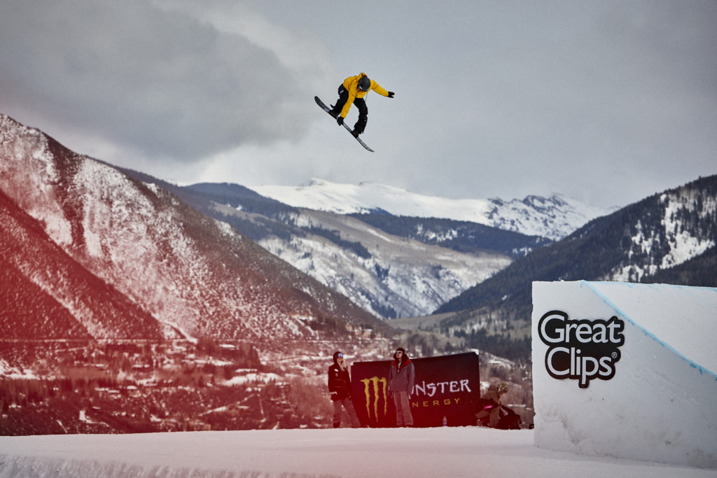 A snowboarder flying over a slope and two people watching below