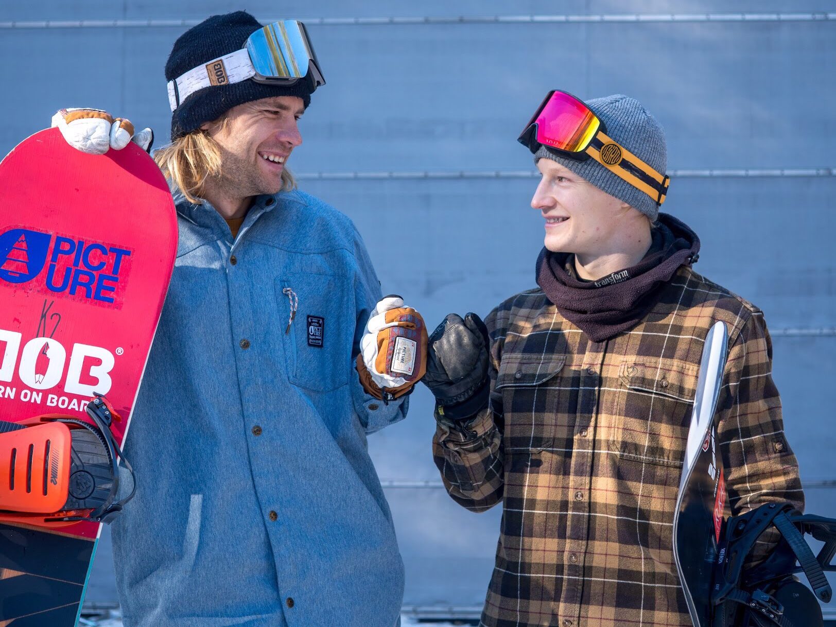 Two snowboarders with glasses looking at each other and smiling 