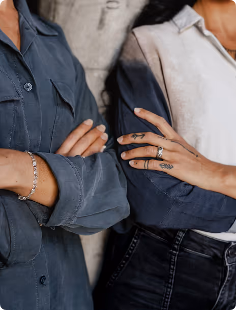Nahaufnahme von zwei verschränkten Armen mit Tattoos und Schmuck.