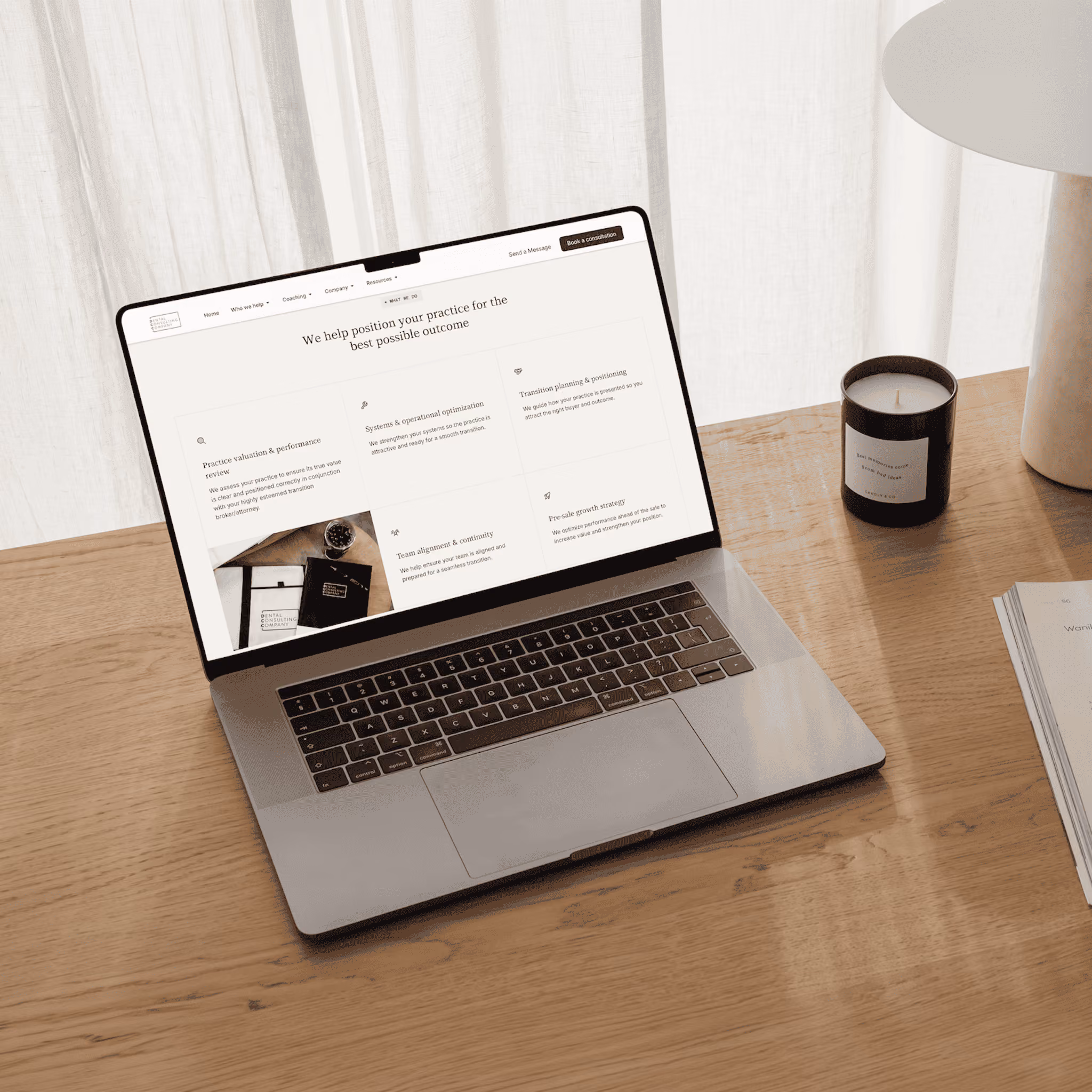 Laptop on wooden desk displaying a website about practice positioning with candle and book nearby.
