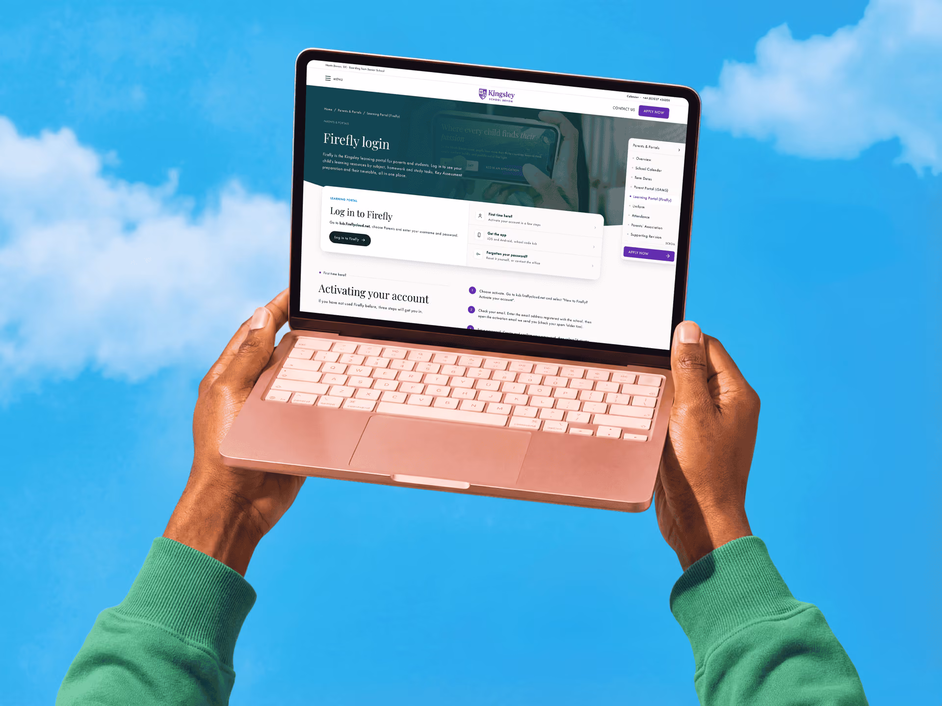 Person wearing a green sweater holding an open pink laptop against a bright blue sky with clouds, displaying the Firefly login page of Kingsley website.