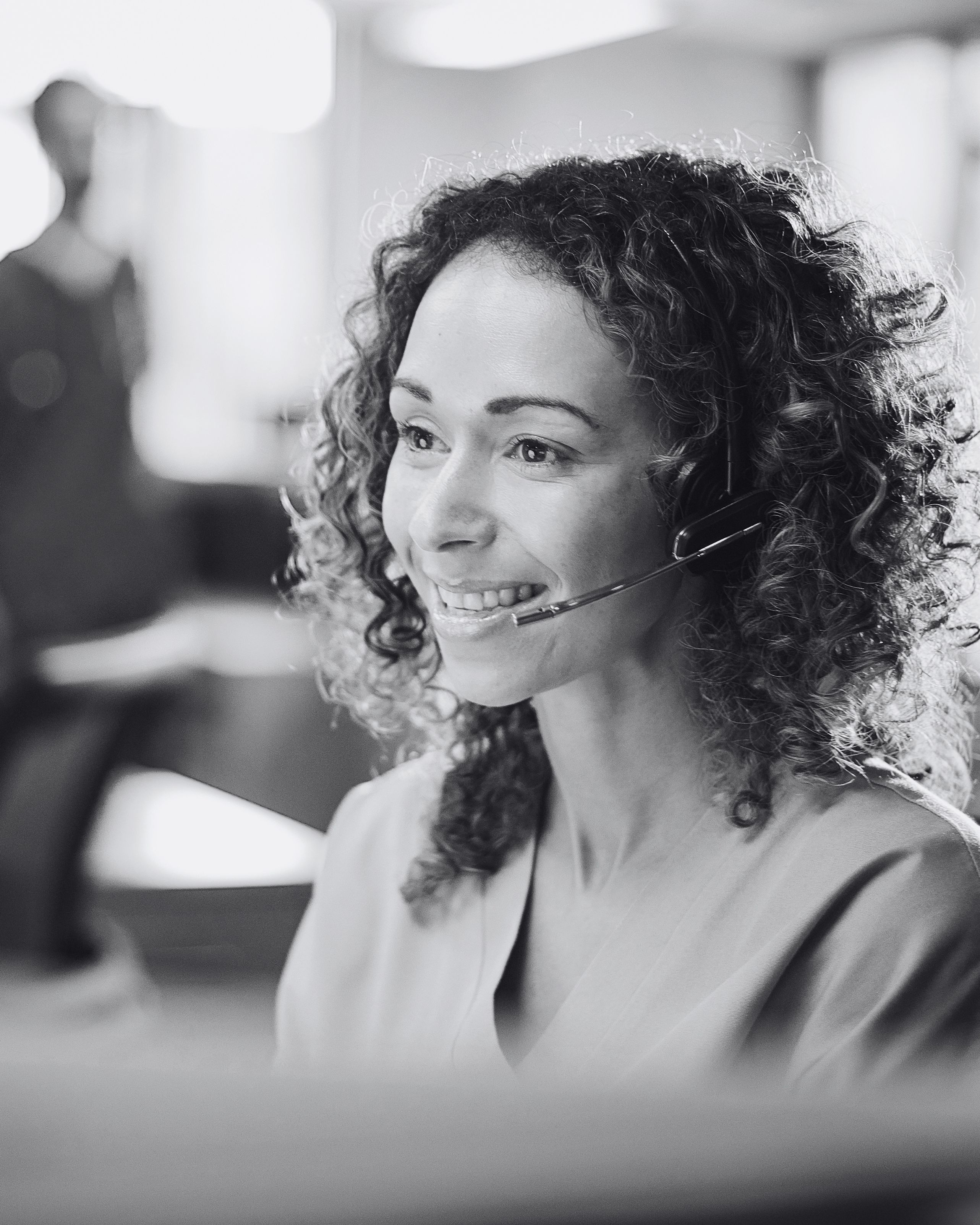 Smiling woman with curly hair wearing a headset in a customer support office.