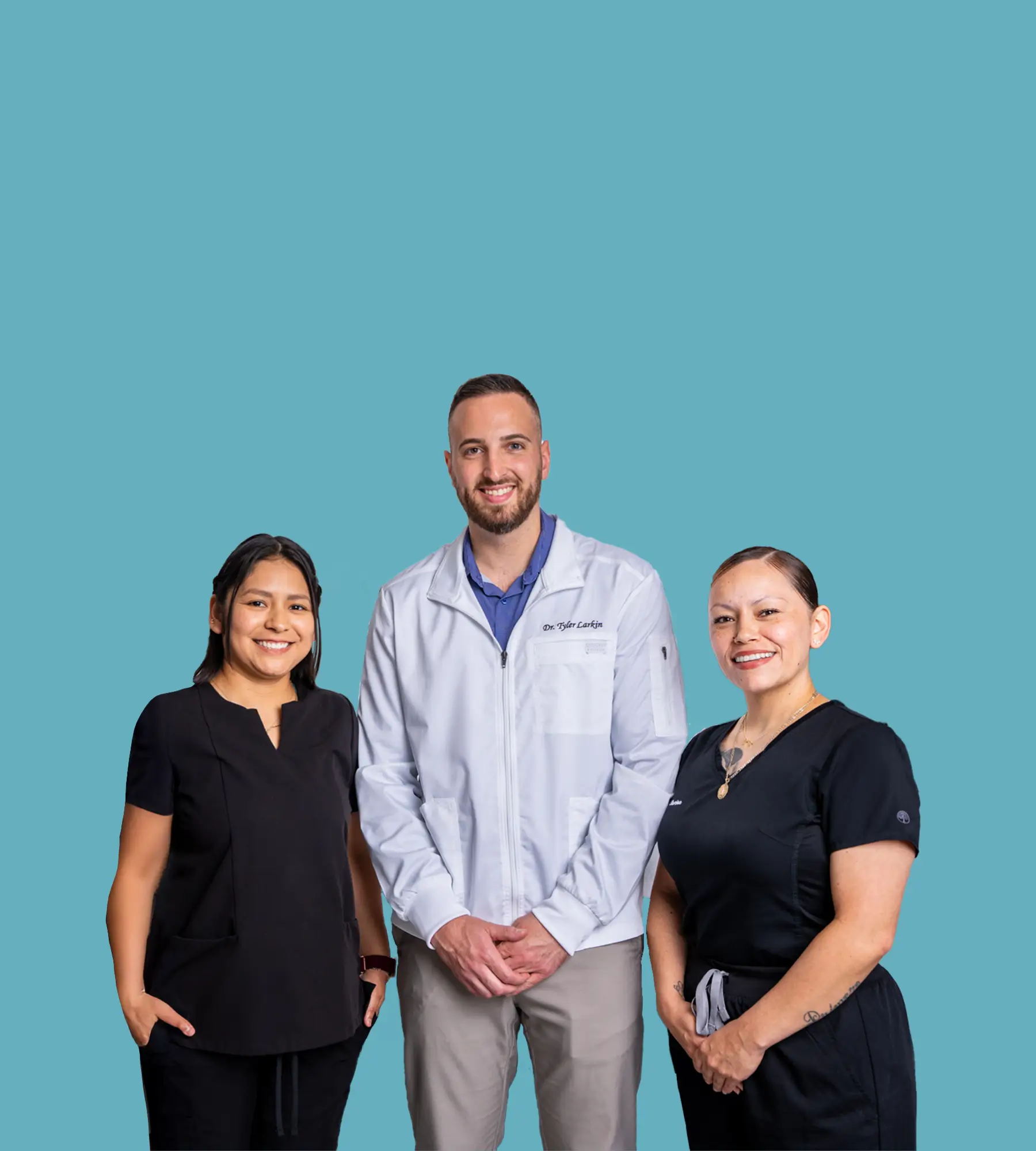 A male dentist stands with two female dental assistants against a plain blue background.