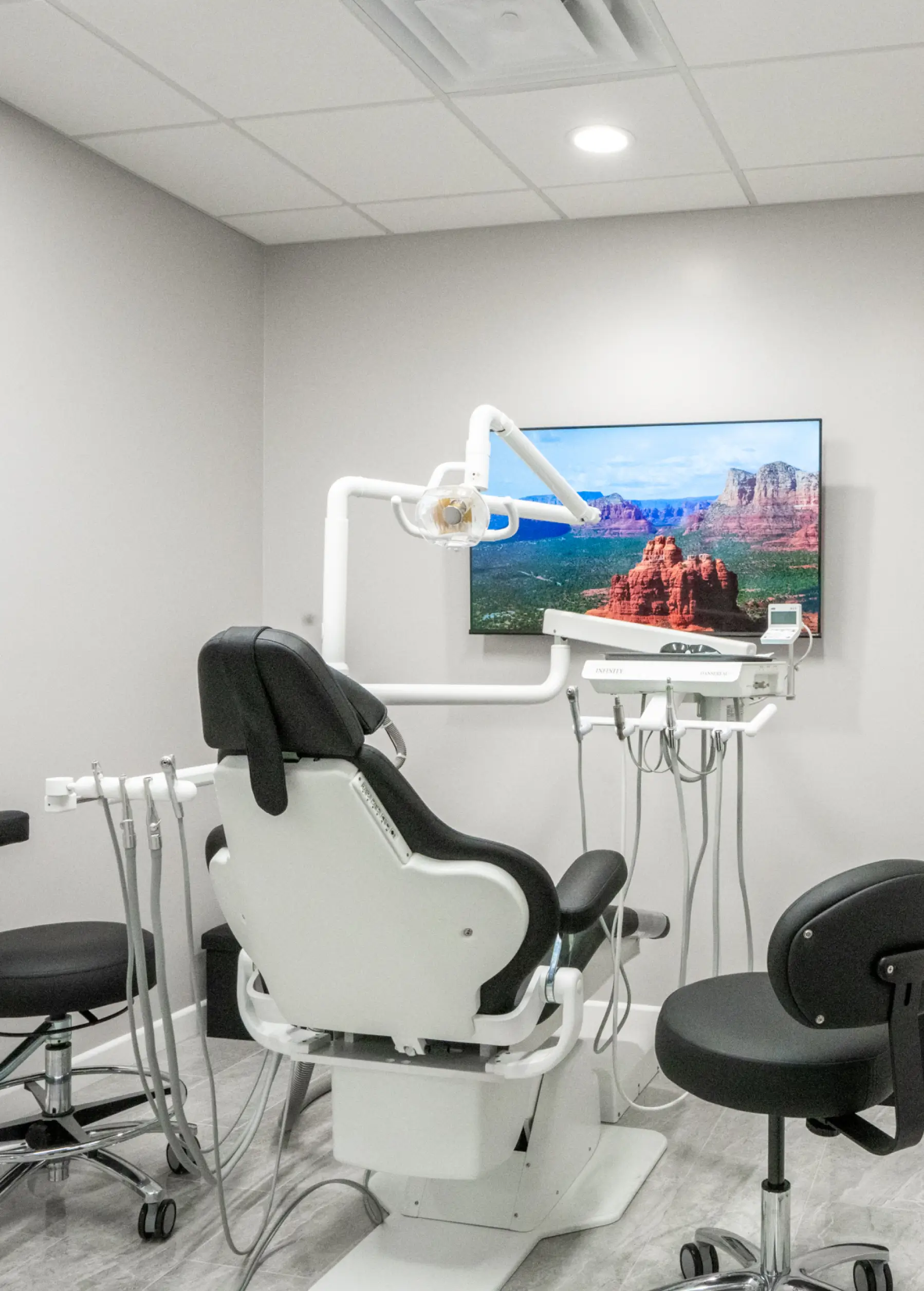Dental examination room with a chair, dental tools, and a wall-mounted screen showing a landscape image.