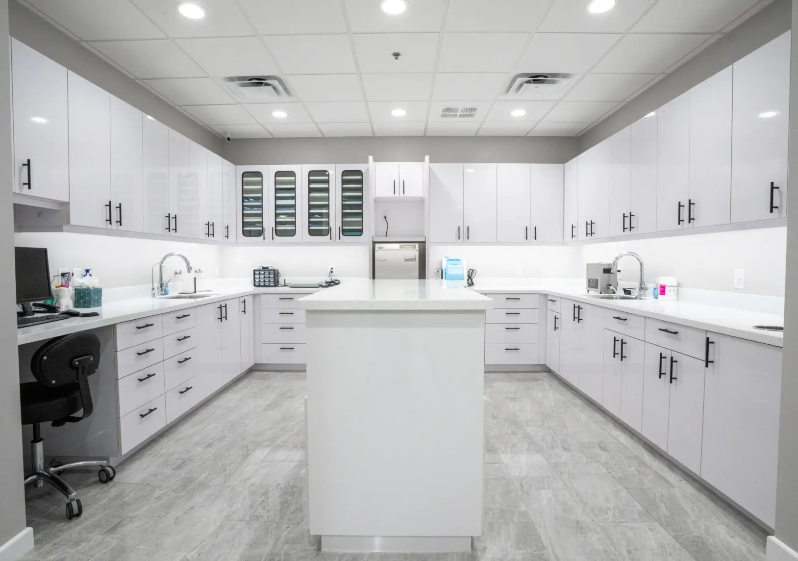 A clean, modern dental office with white cabinetry, two sinks, and equipment on the countertops.