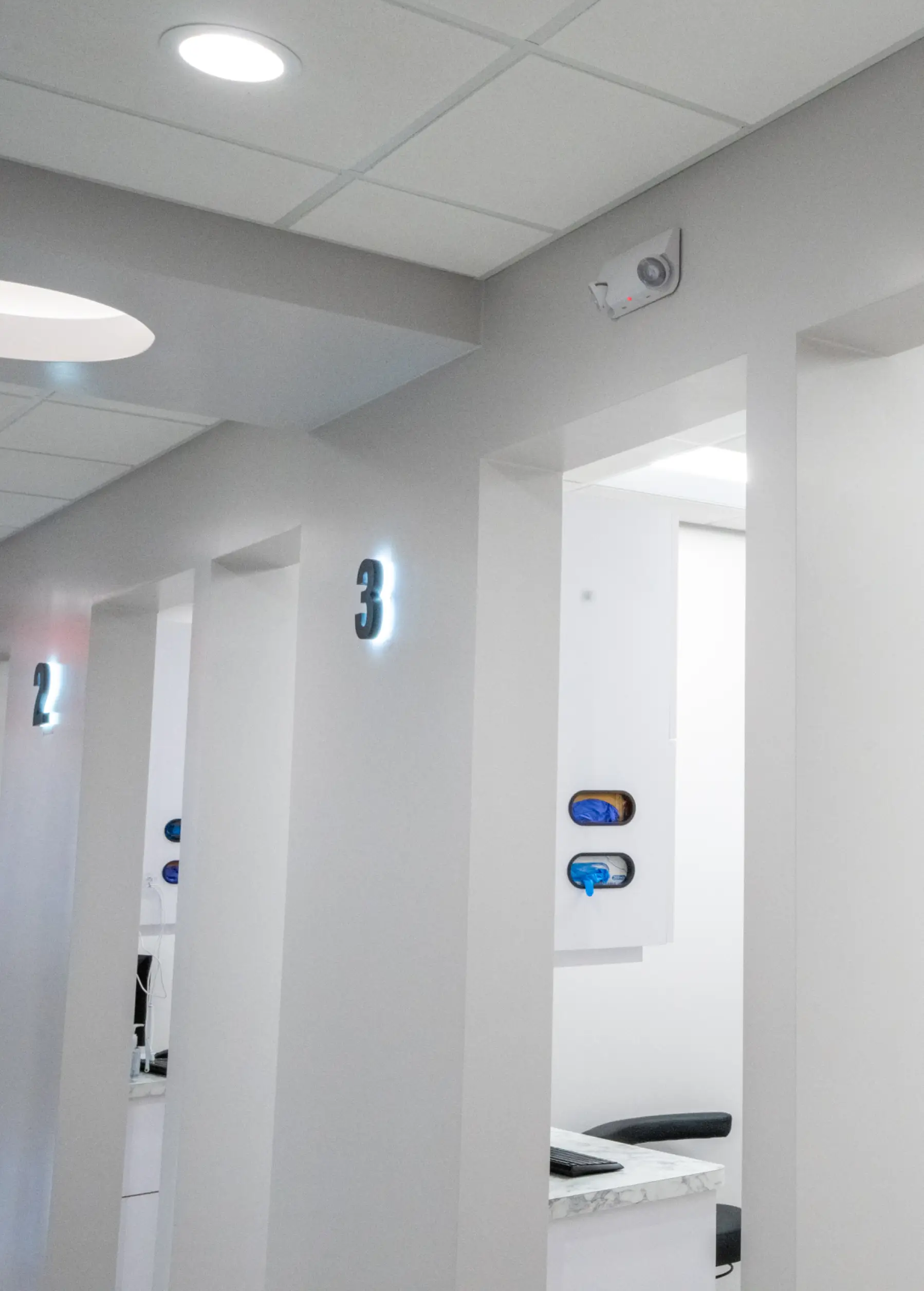 Hallway in a modern office with numbered cubicles and bright overhead lighting.