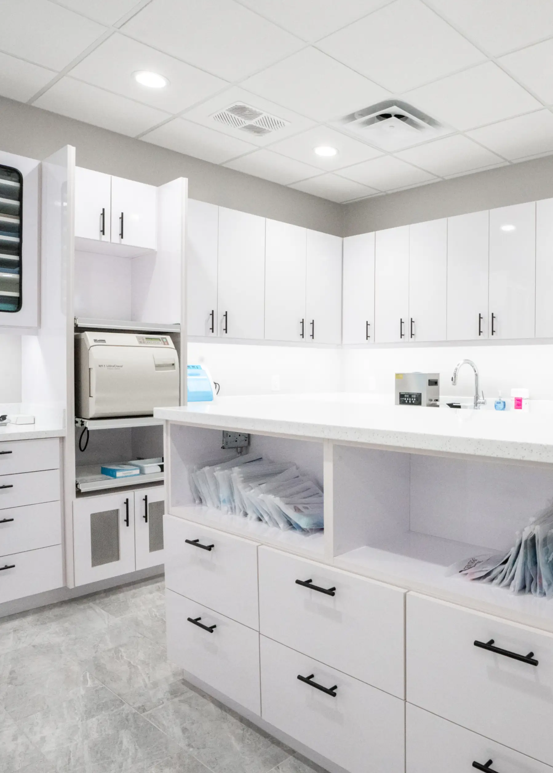 A clean, organized dental office showing cabinets, a dental autoclave, and neatly stacked dental supplies.