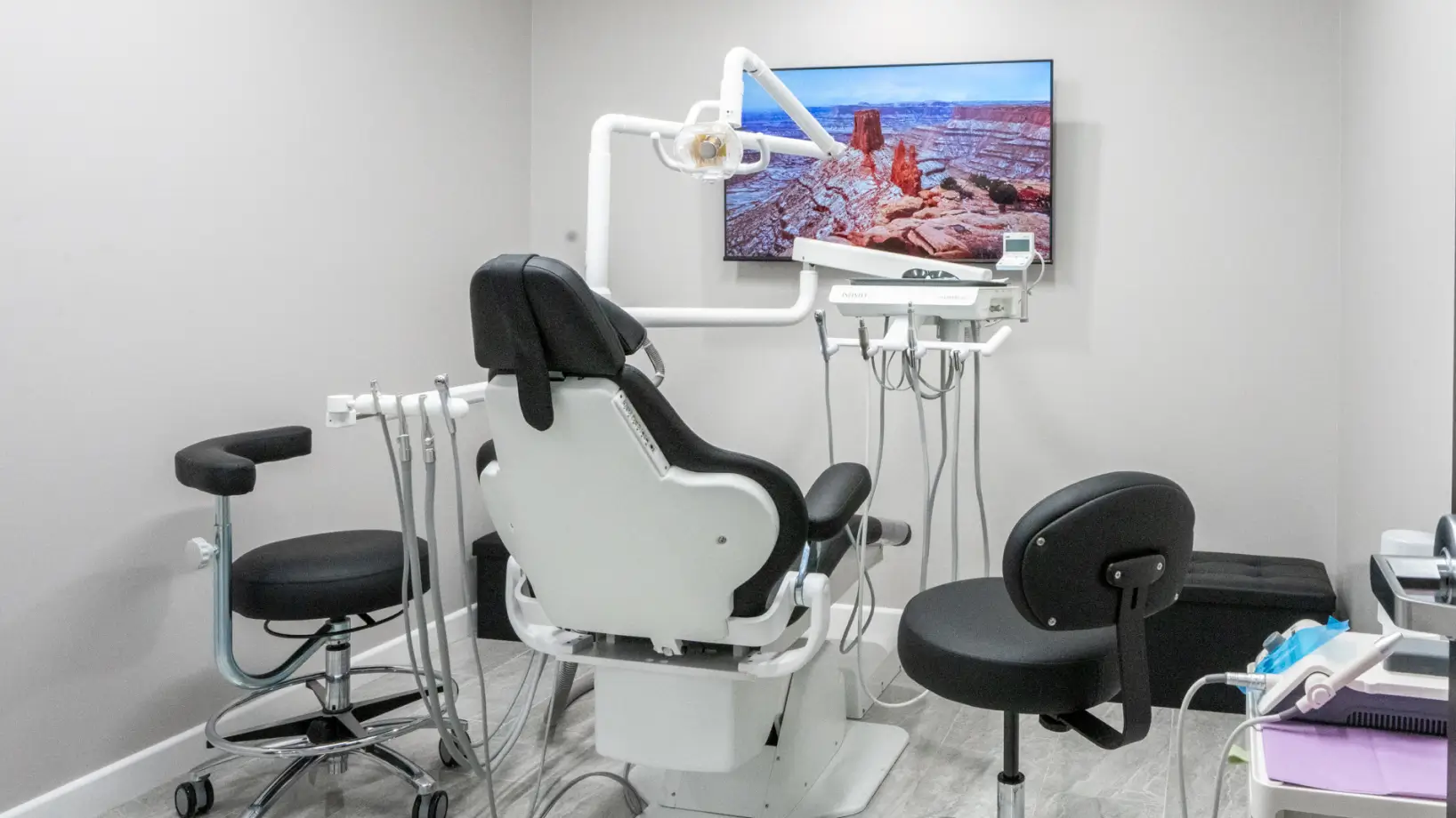 A modern dental treatment room with a chair, dental tools, and a scenic photo on the wall.
