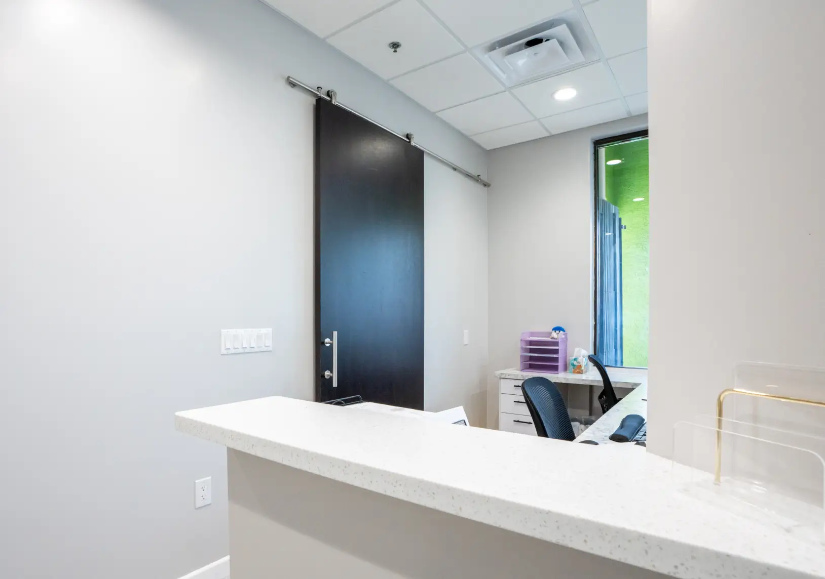 A small, tidy office reception with a desk, two chairs, and a sliding door.