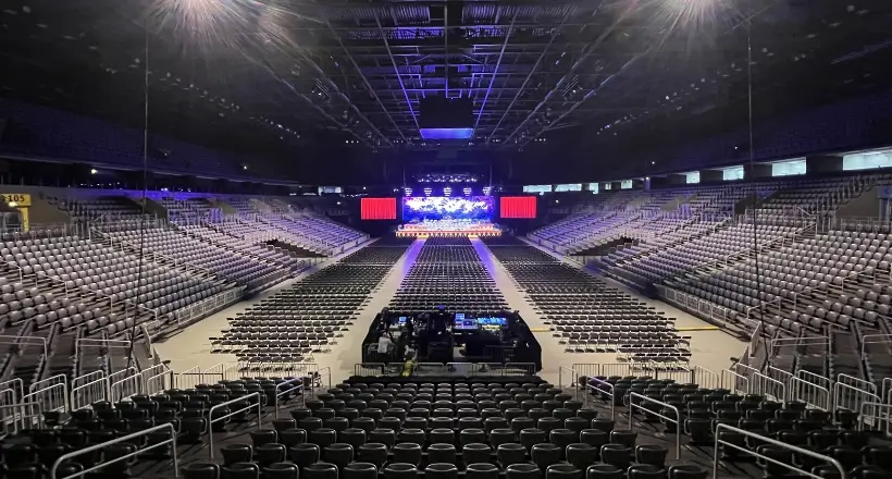 Interior view of a large, empty concert arena with rows of seats facing a lit stage, ready for the show.