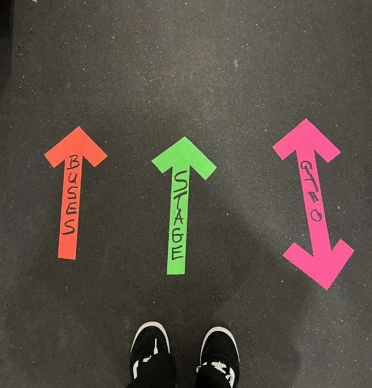 Close-up of brightly coloured fluorescent labeled arrows on the floor, pointing to 'Buses', 'Stage', and way out for technical crew direction.