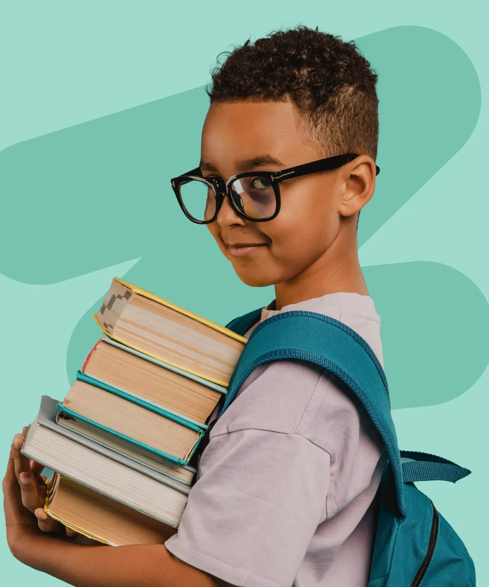 A young boy with glasses holding a stack of books.