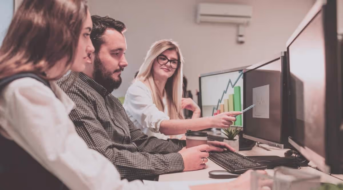 Three persons are sitting in front of computers and looking at a graph on computer screen - Blog - Autymate