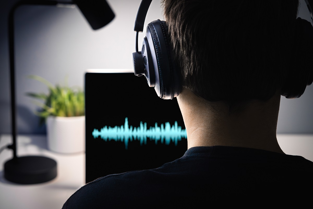 Person wearing headphones analyzing an audio waveform on a computer screen, illustrating AI voice analysis for fraud detection