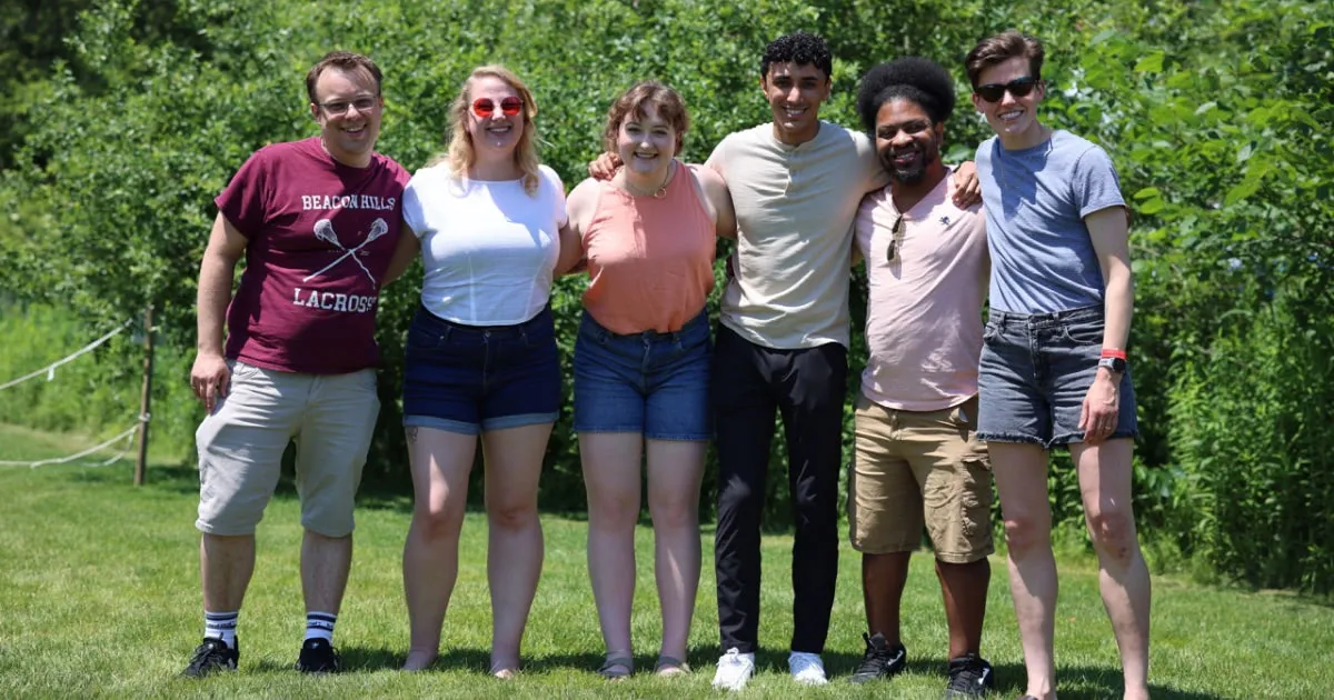 Group of friends standing together outdoors, smiling with arms around each other