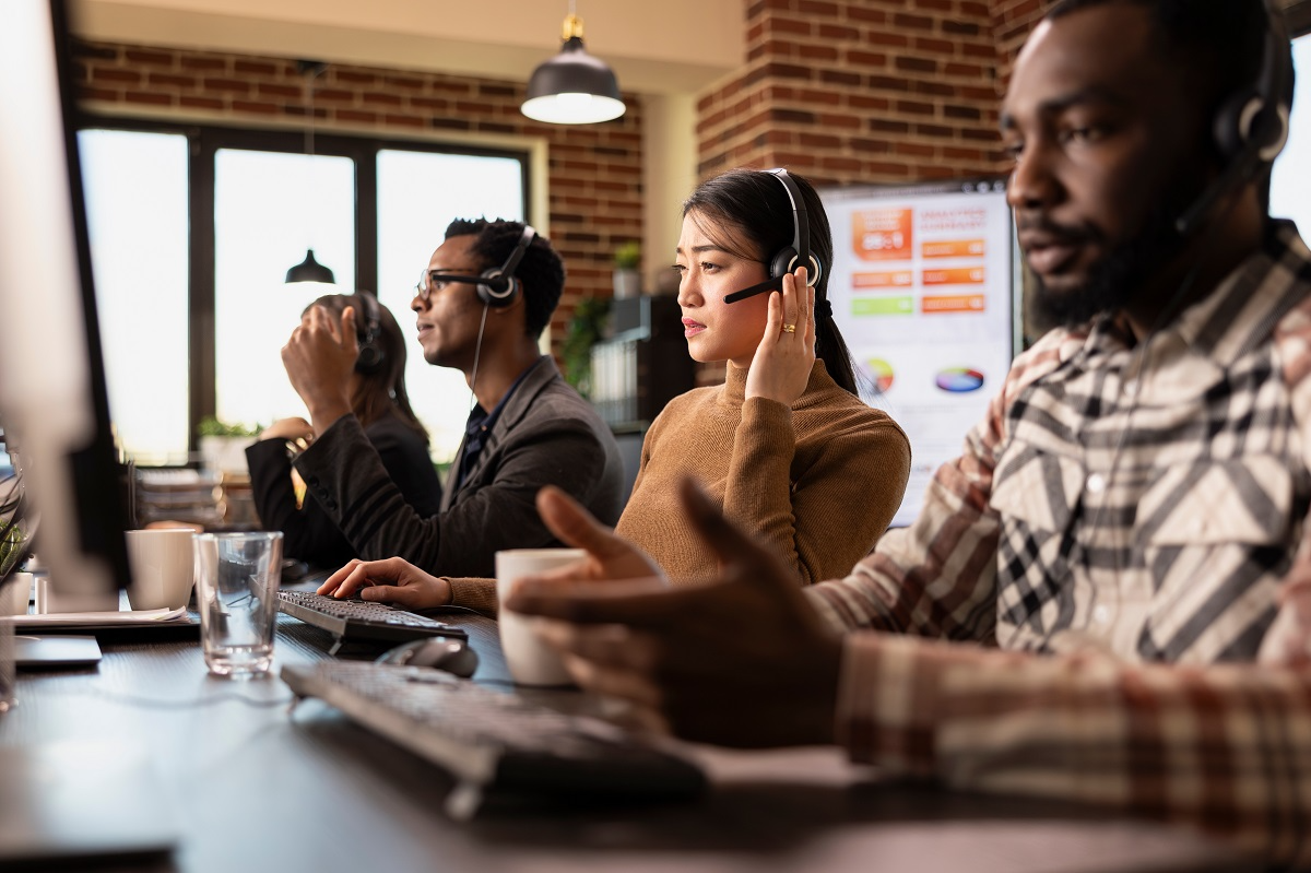 Diverse customer support team working in a modern call center with headsets and live analytics dashboards in the background