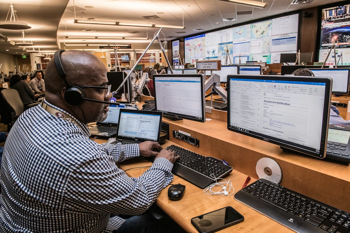 Contact center agent working in a monitoring and operations center with multiple screens displaying real-time customer service data.