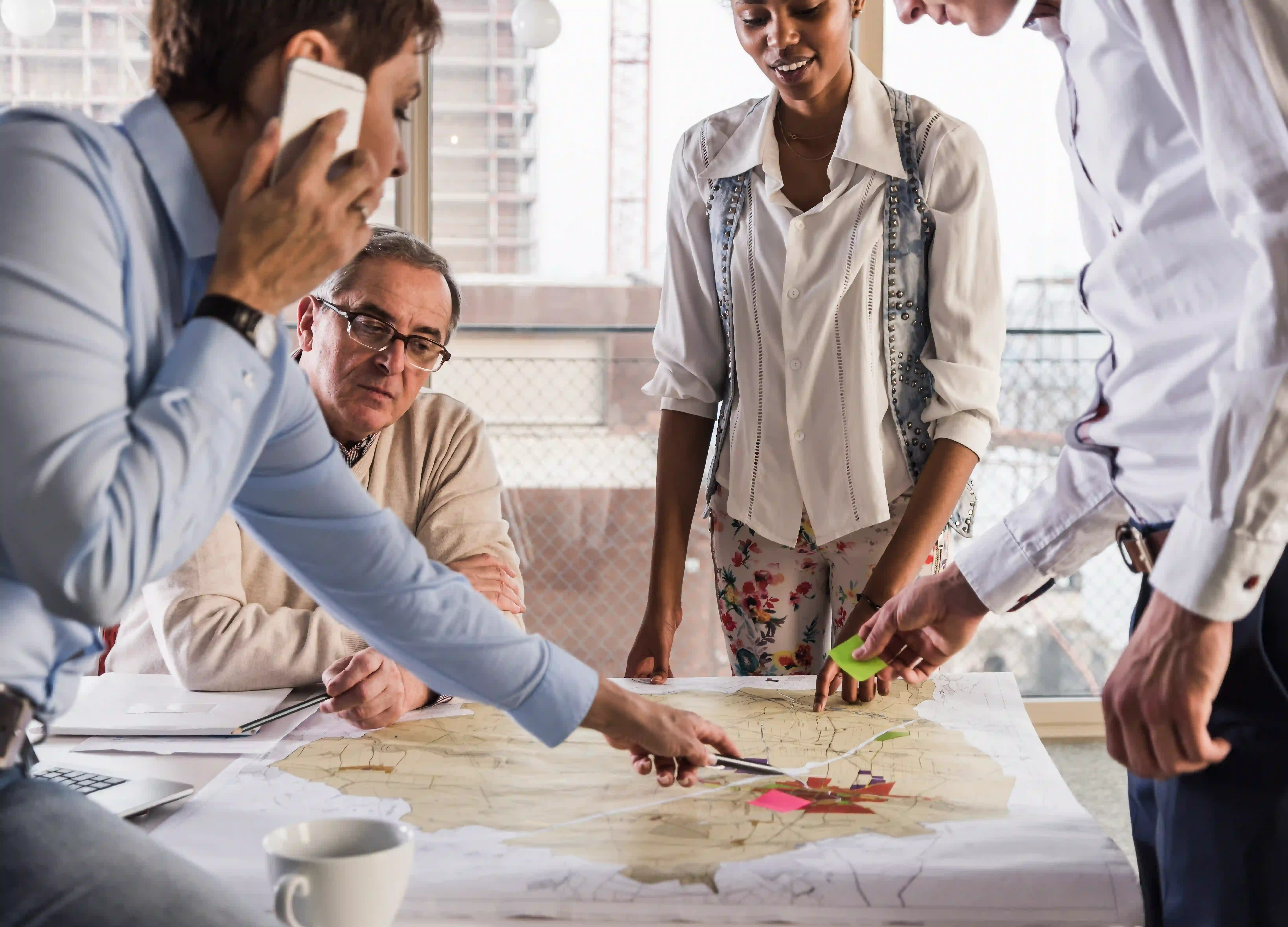A diverse group of individuals gathered around a large map, discussing and pointing at various locations.