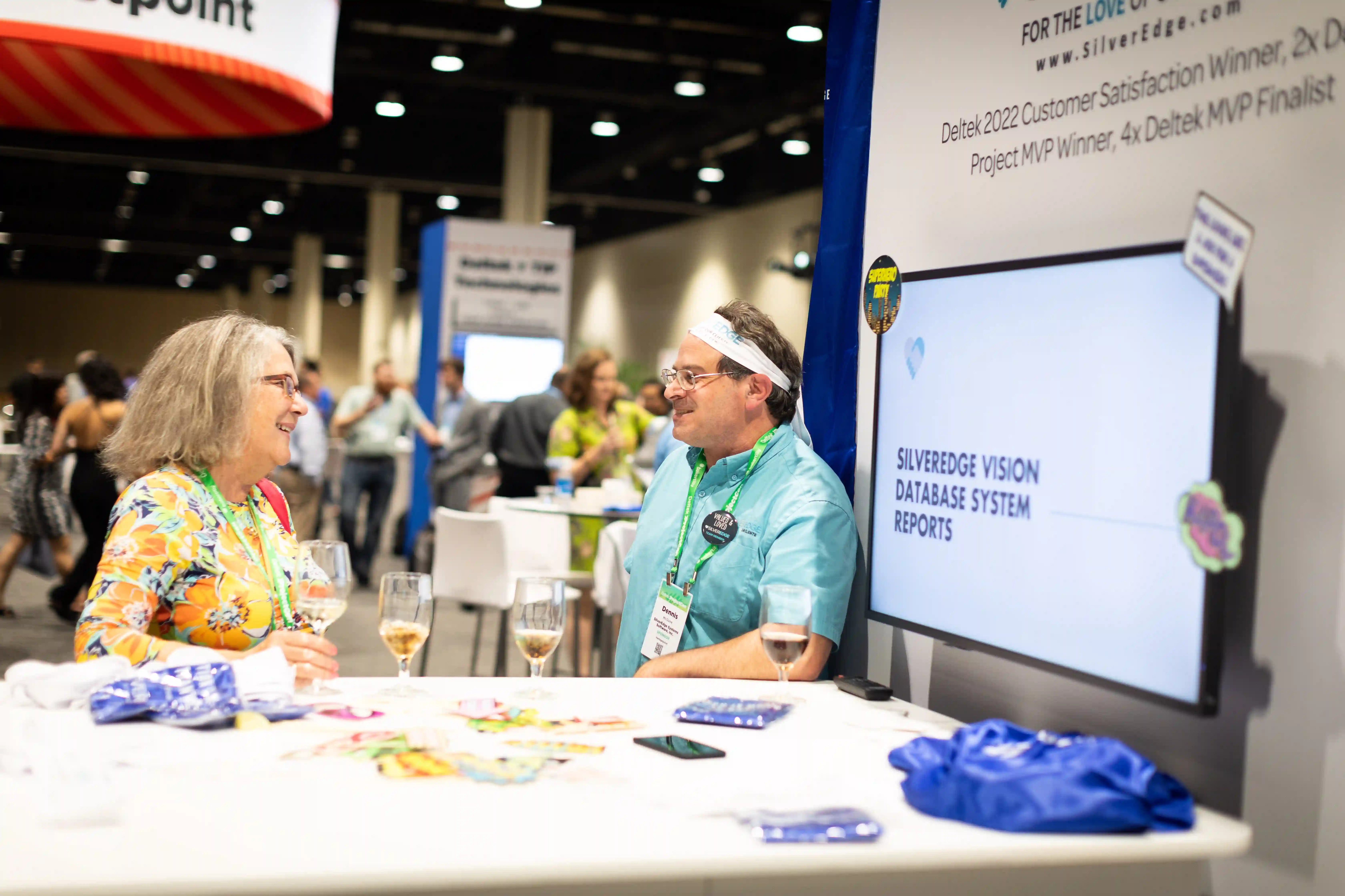 A man and woman engaged in conversation while seated at a table during a convention event.