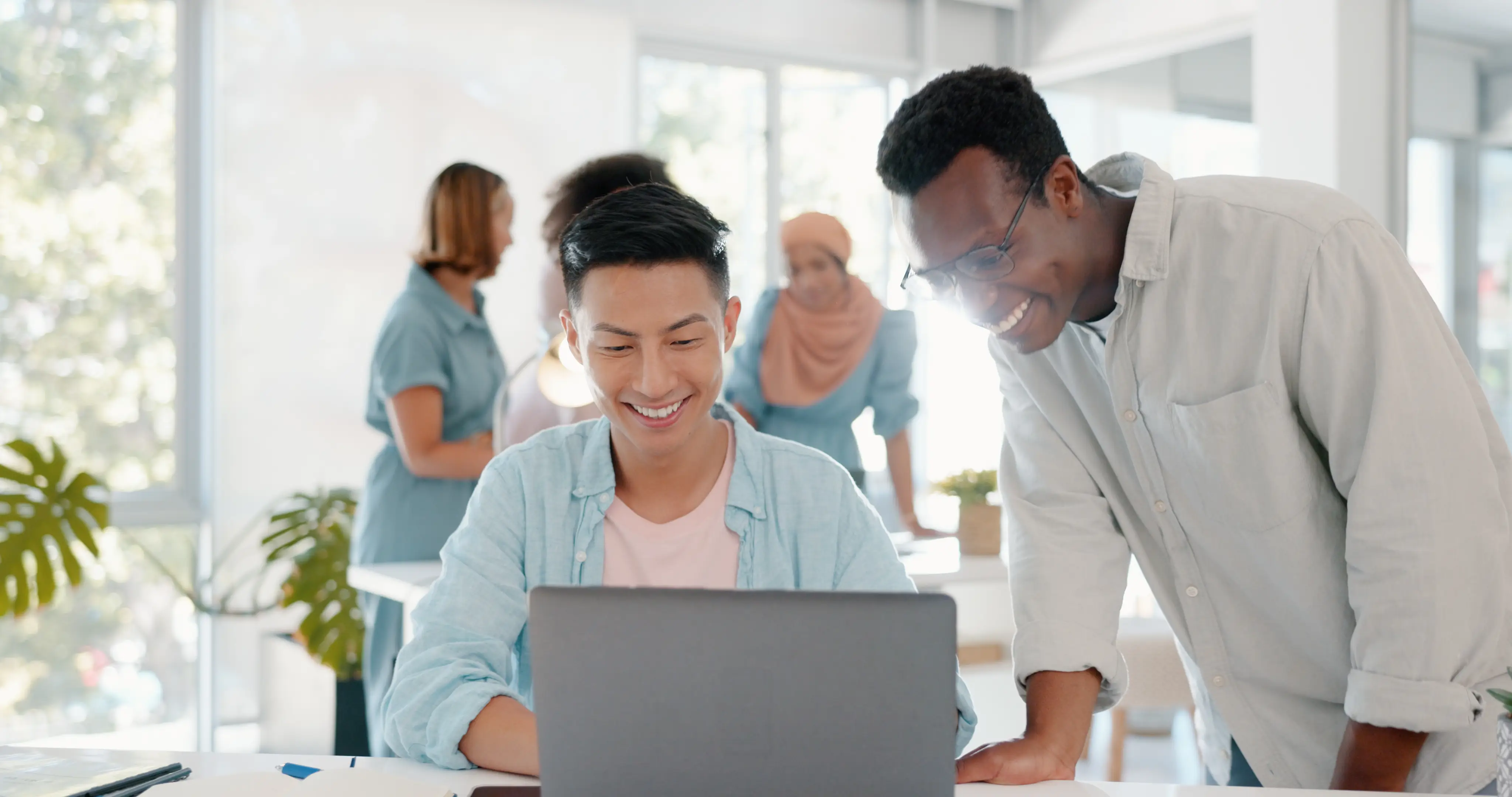 Two men and a woman smile together while collaborating on a laptop, showcasing teamwork and engagement in their work.