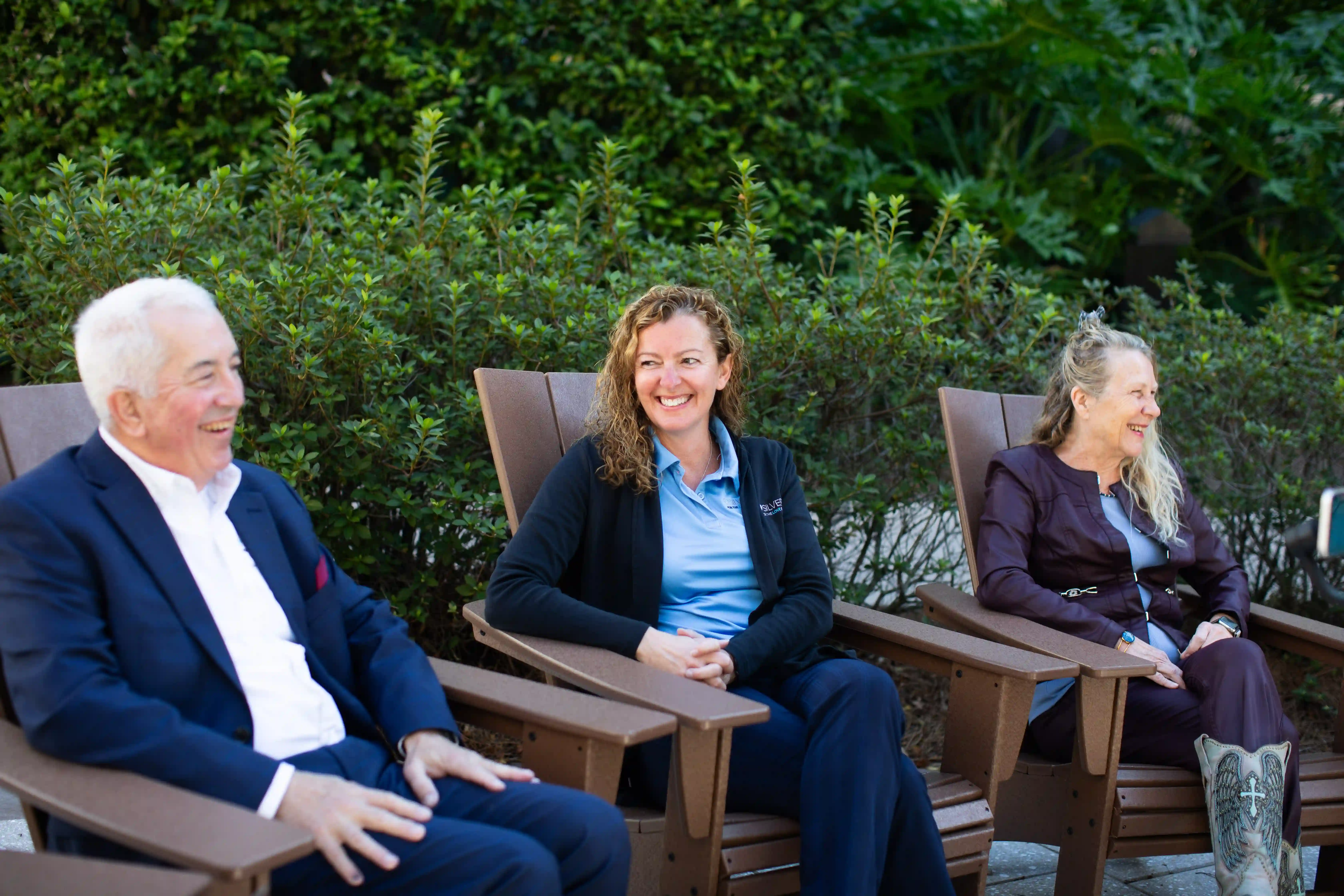 A diverse group of individuals seated in chairs outdoors, enjoying a pleasant day in a communal setting.