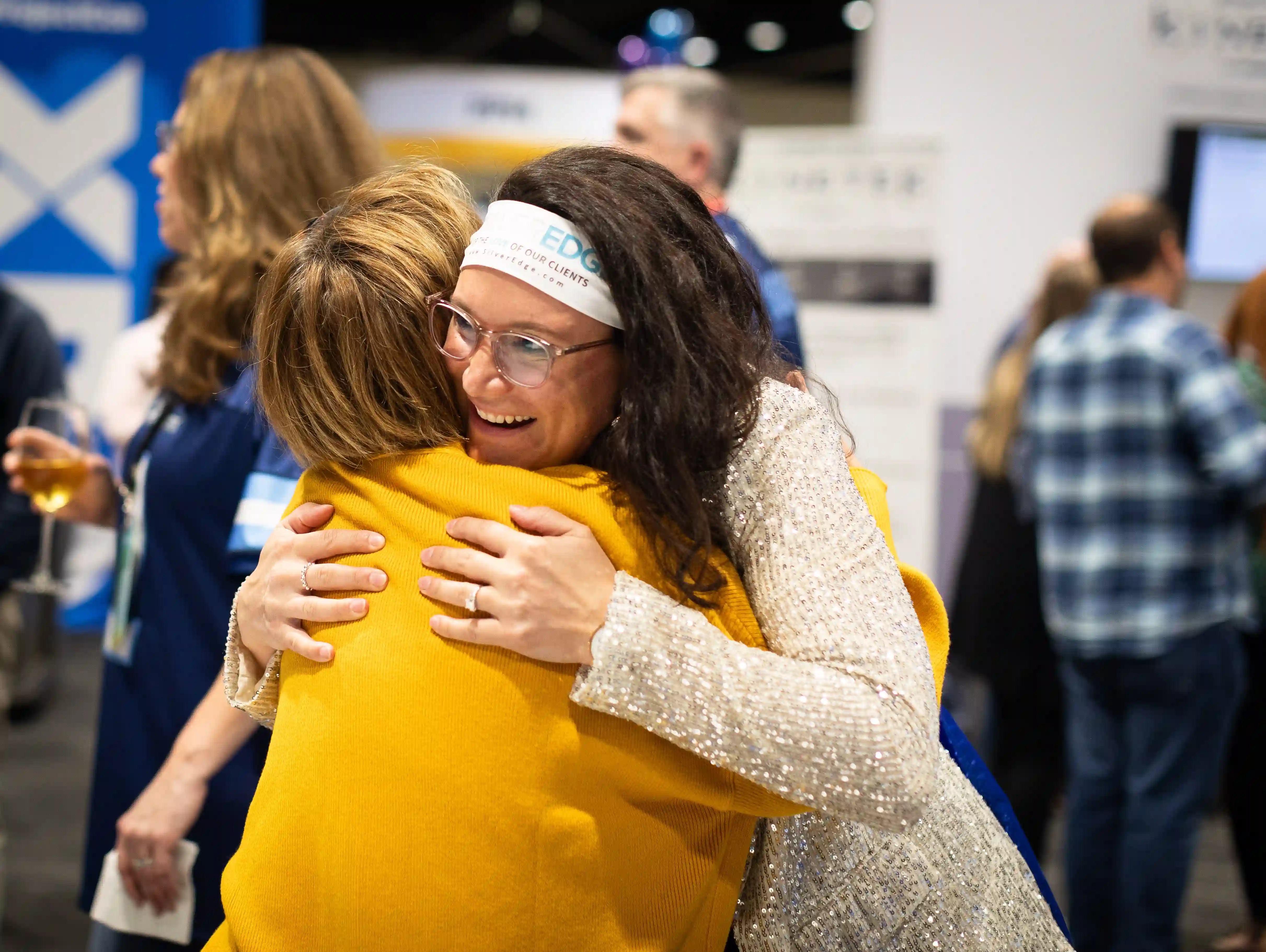 Two women embrace warmly at an event, showcasing friendship and joy in a celebratory atmosphere.