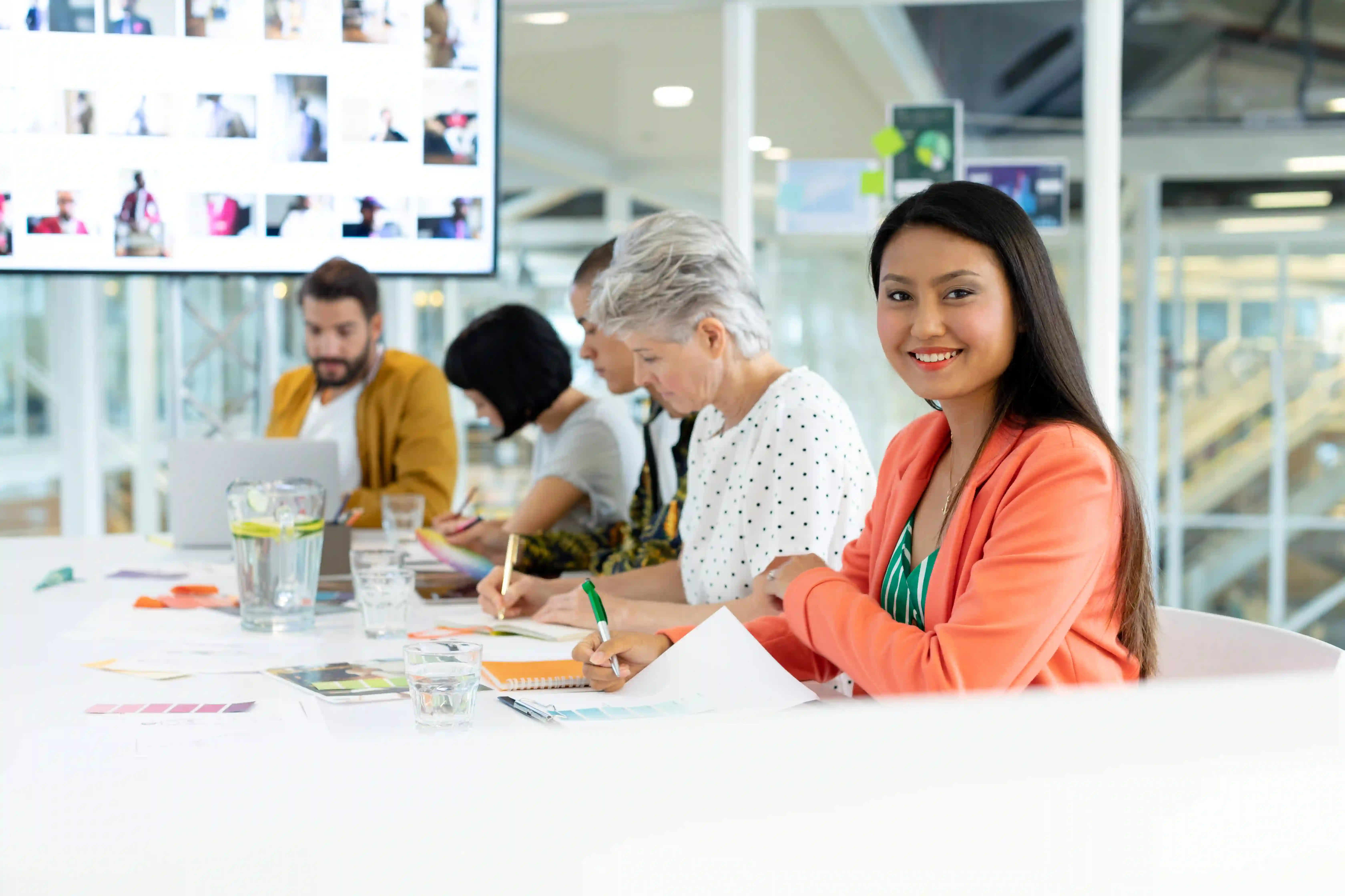 A diverse group of individuals working and a main woman on the image smiling to the camera.