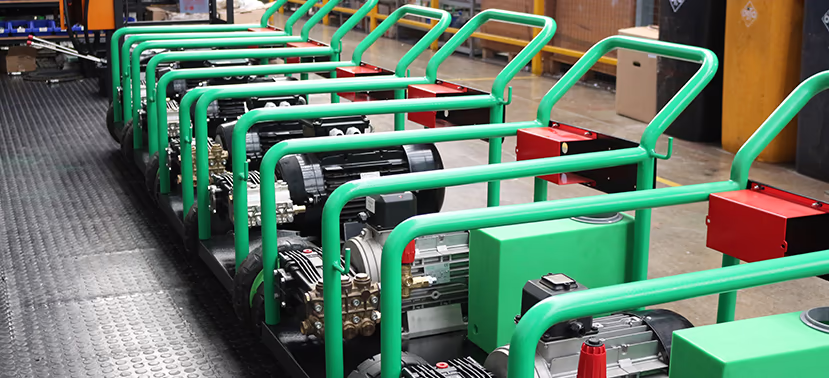 A row of green high-pressure washers lined up on an assembly floor.