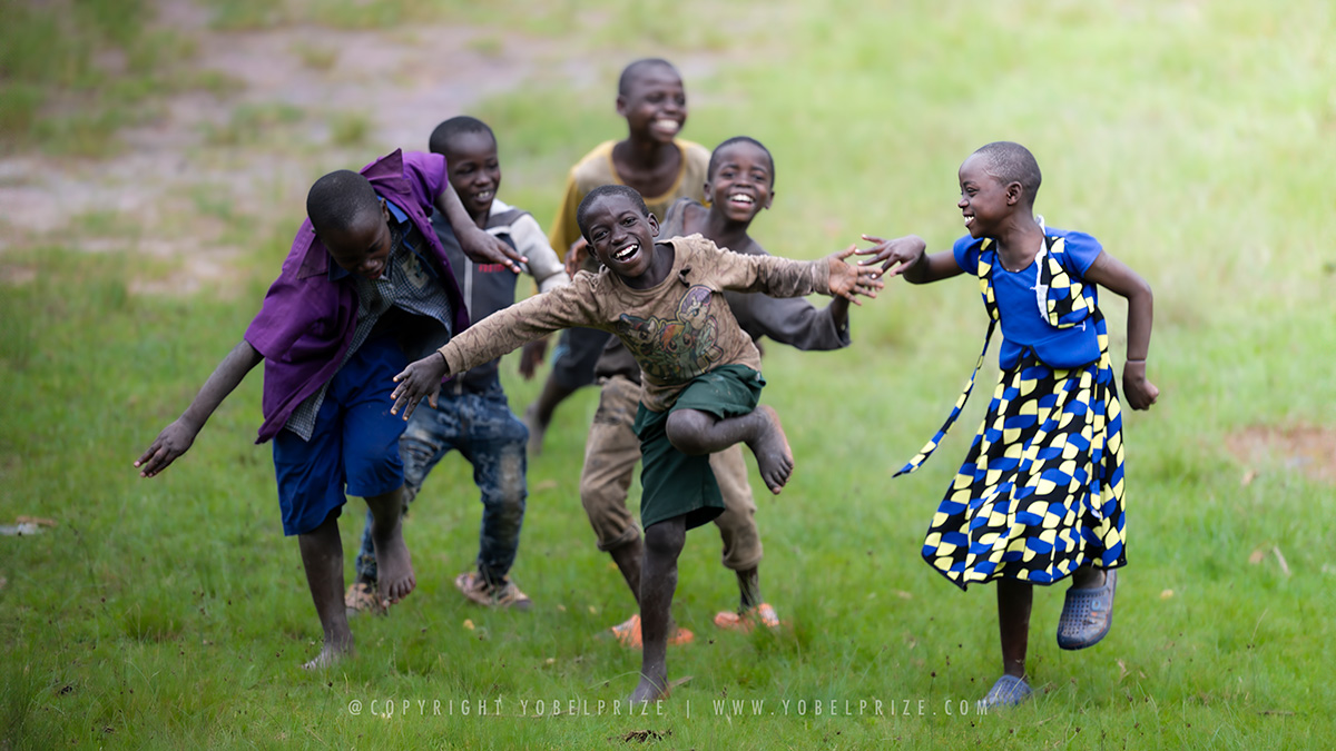 A joyful group of Ugandan children running barefoot, smiling and playfully chasing each other, captured in a moment of pure, carefree happiness on vibrant green grass.