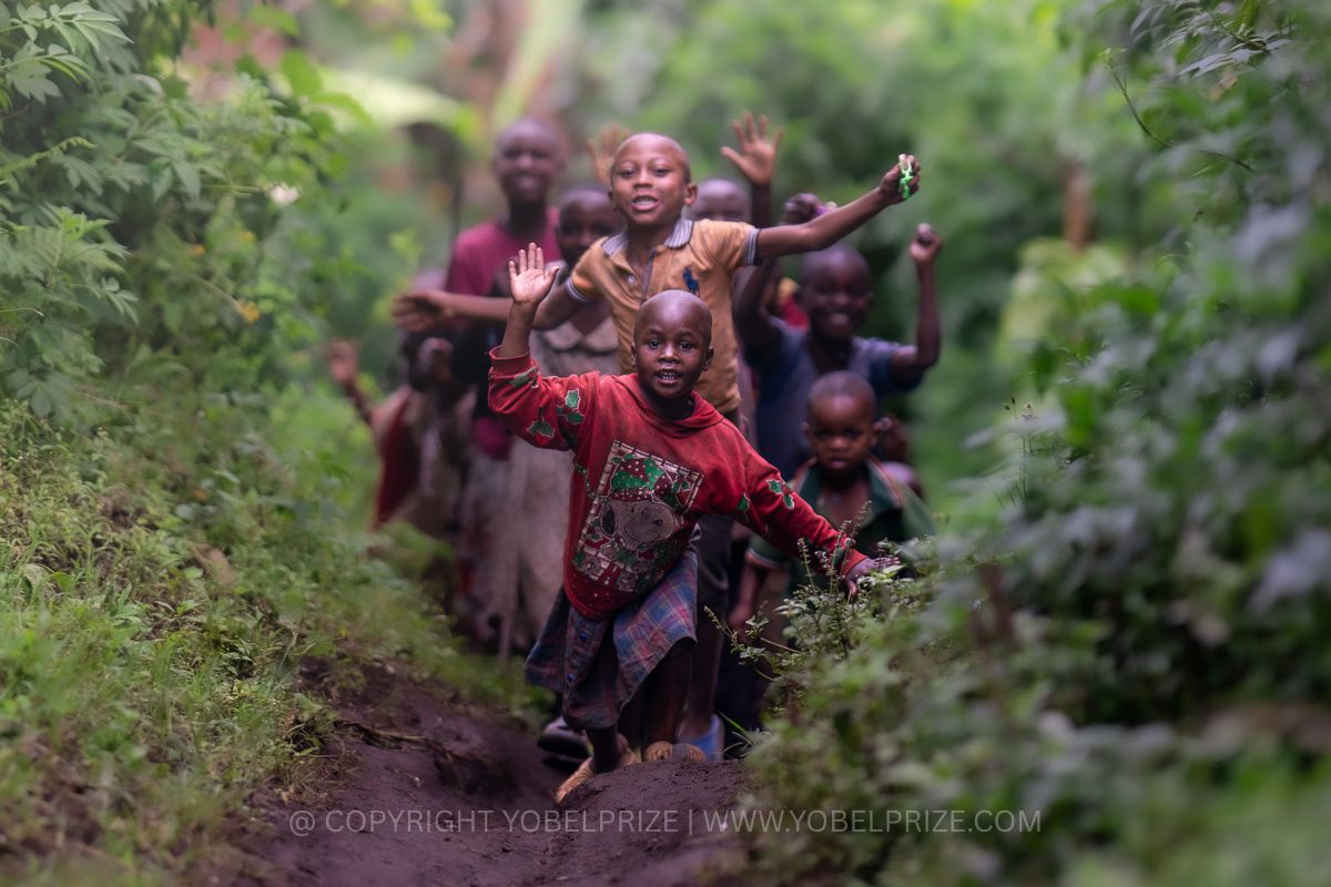 Joyful Ugandan children running and waving enthusiastically down a verdant forest path, capturing vibrant energy and warm smiles.