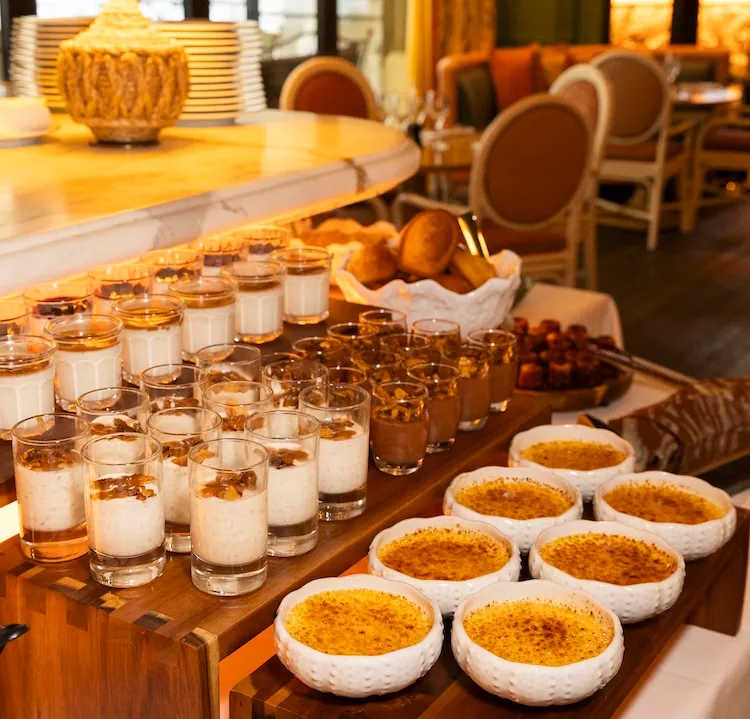 Plateau de desserts dans notre restaurant brunch à deauville, incluant des crèmes brûlées dans des bols blancs, des verrines de crème et mousses, disposés sur une table en bois dans un restaurant.