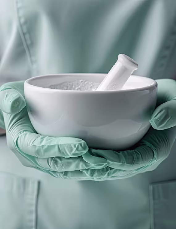 Person wearing green medical gloves holding a white mortar and pestle.