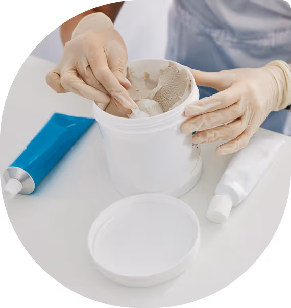 Person in a white robe gently touching their bare foot standing on a gray textured bath mat beside a woven basket.
