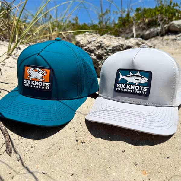 Six Knots water-resistant snapback hats resting on sandy beach in North Carolina – durable boating hats for sun and surf conditions