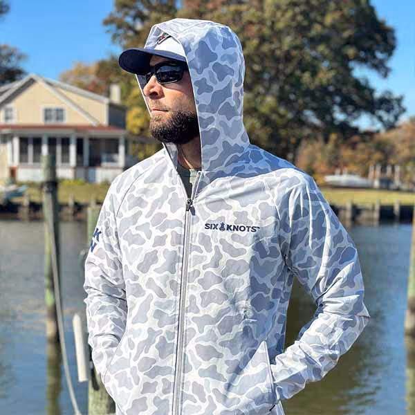 Man wearing hooded Six Knots Coastal Camo Rain Jacket on a dock — lightweight, waterproof fishing and boating outerwear ideal for anglers, sailors, and coastal lifestyle enthusiasts