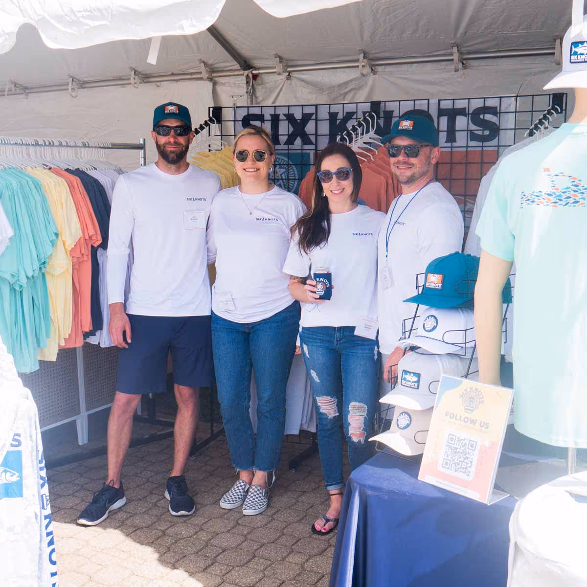 Two men and two women standing together in the Six Knots booth at the Bay Bridge Boat Show, showcasing boating and fishing apparel and representing the brand.