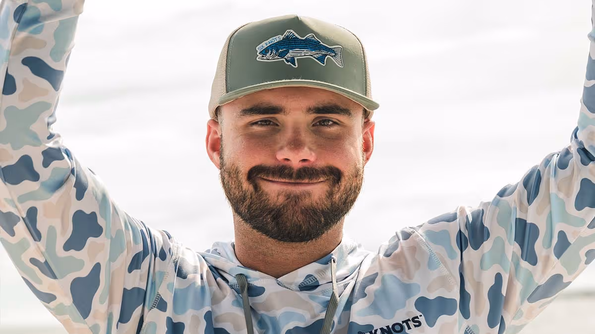 Man wearing a Six Knots Trophy Season snapback and performance hoodie, showcasing stylish boating and fishing apparel with a confident smile
