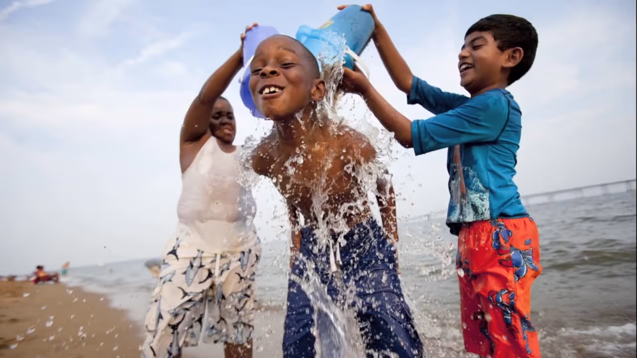 Two boys pouring water over a friend’s head while playing on a sandy Chesapeake Bay beach