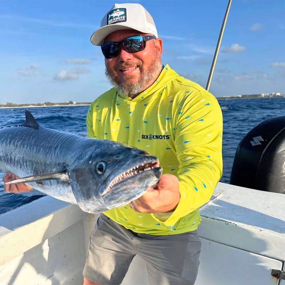 Man holding a freshly caught fish on the deck of his boat, wearing the Six Knots Dorado Performance Hoodie — moisture-wicking, lightweight fishing apparel