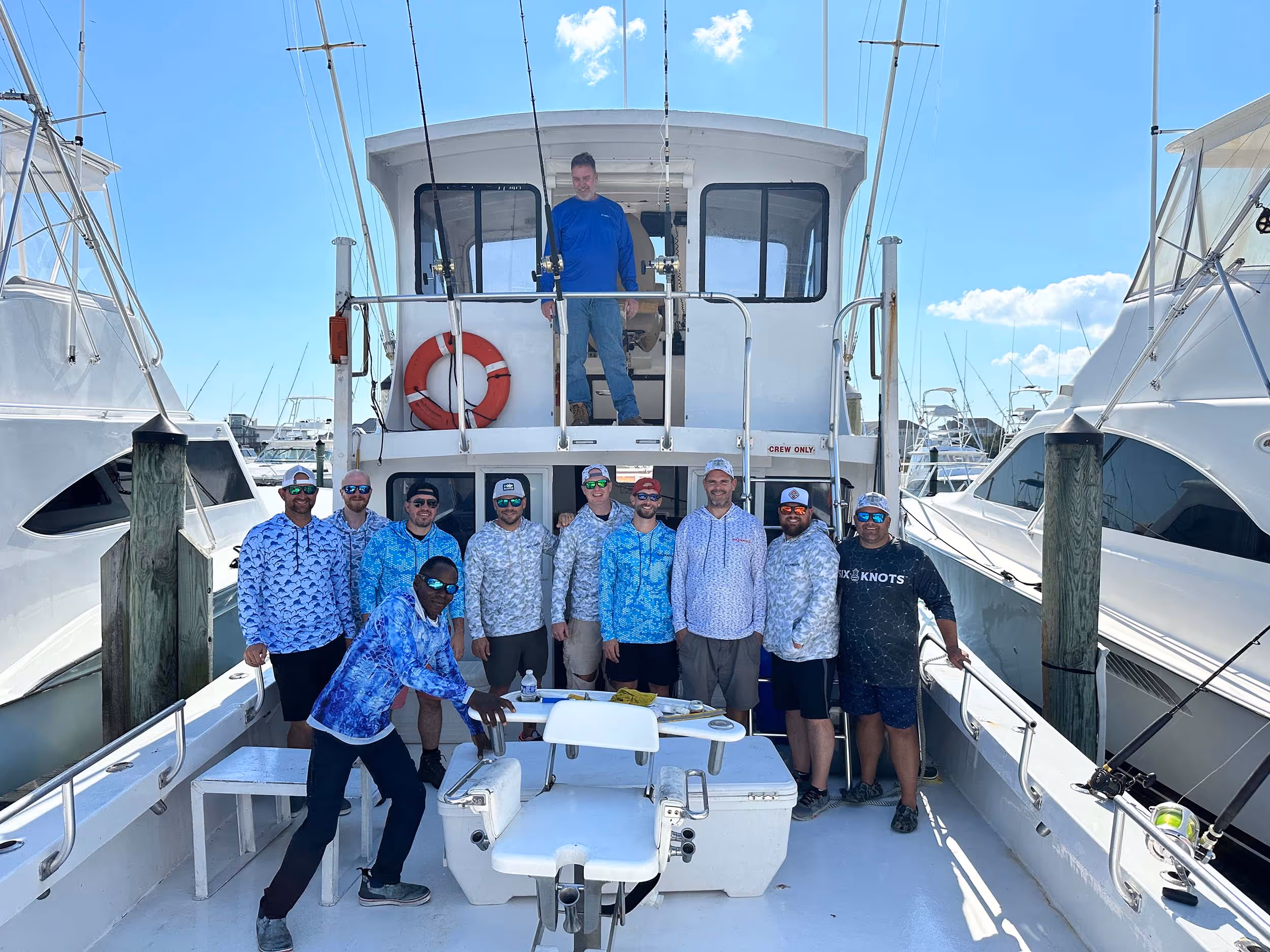 Friends on a fishing boat wearing Six Knots apparel, posing and smiling proudly for a group photo.