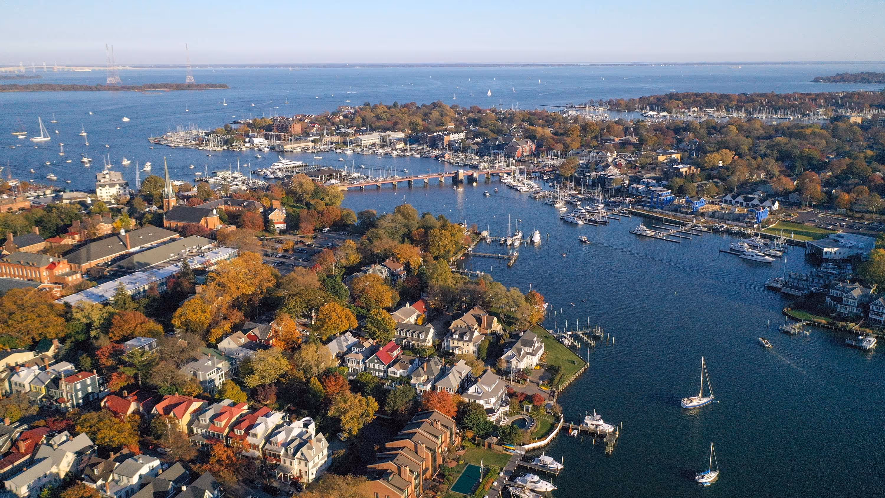 Aerial view of sailboats gliding through the calm waters of the Chesapeake Bay surrounded by golden autumn foliage