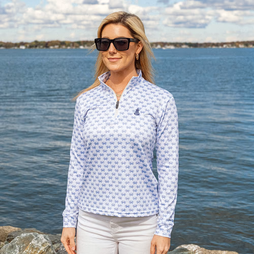 Woman wearing a Performance Quarter Zip from Six Knots while standing in a marina in front of water