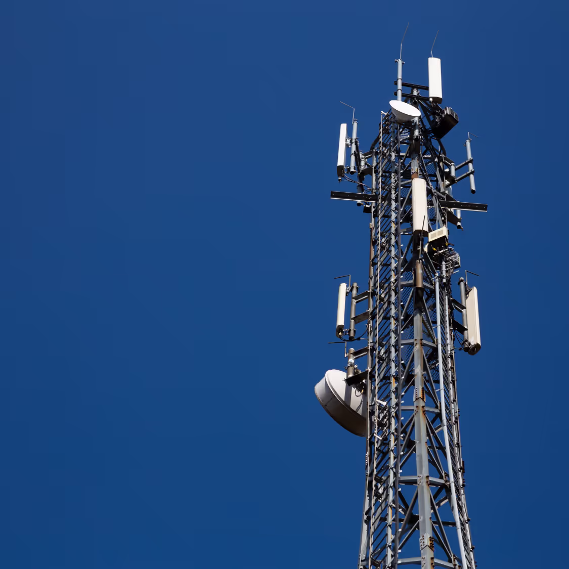 Telecommunications tower with antennas and equipment against a clear blue sky, symbolizing wireless connectivity and communication networks.