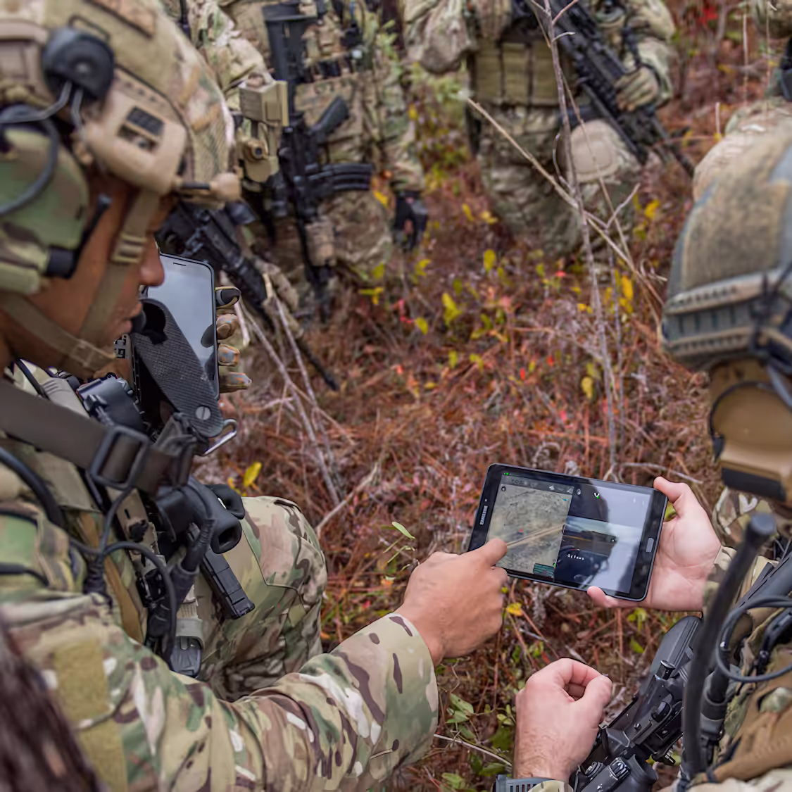 Soldiers using advanced digital tablets and communication gear in a field operation, showcasing modern military technology integration.