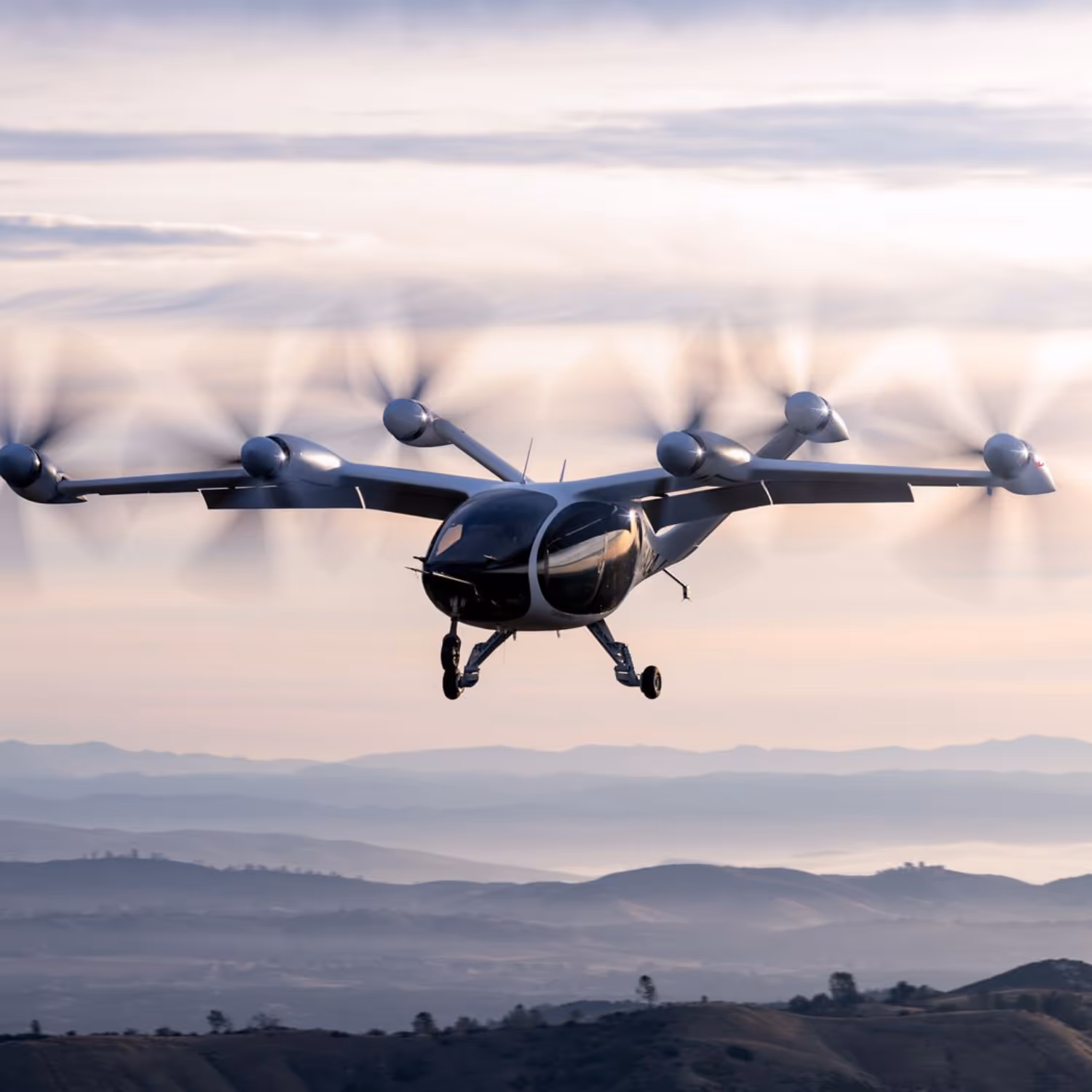 Electric vertical takeoff and landing (eVTOL) aircraft flying over mountainous terrain during sunset, featuring multiple rotors and a futuristic design.