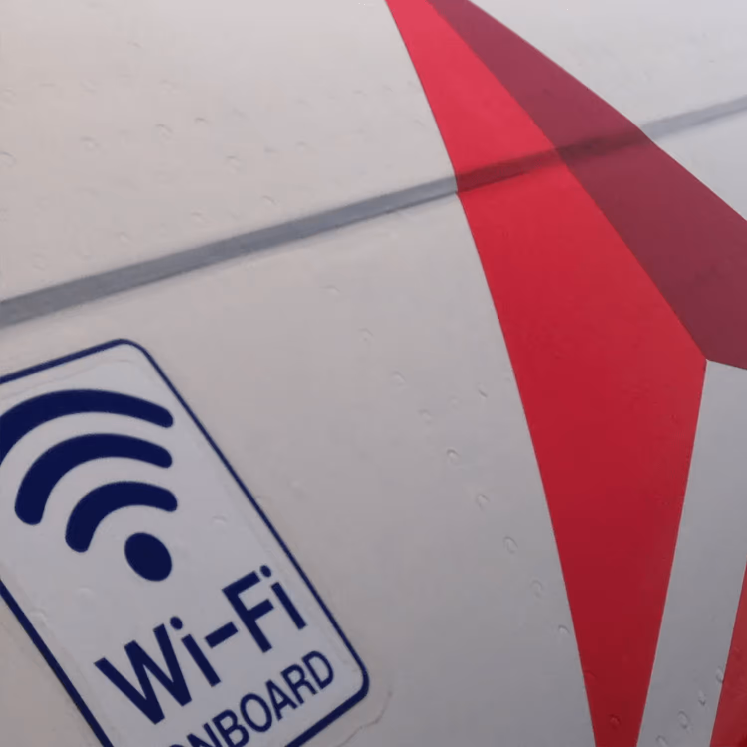 Close-up view of an aircraft fuselage with a Wi-Fi onboard sticker, featuring aerodynamic detailing and part of a red painted logo.