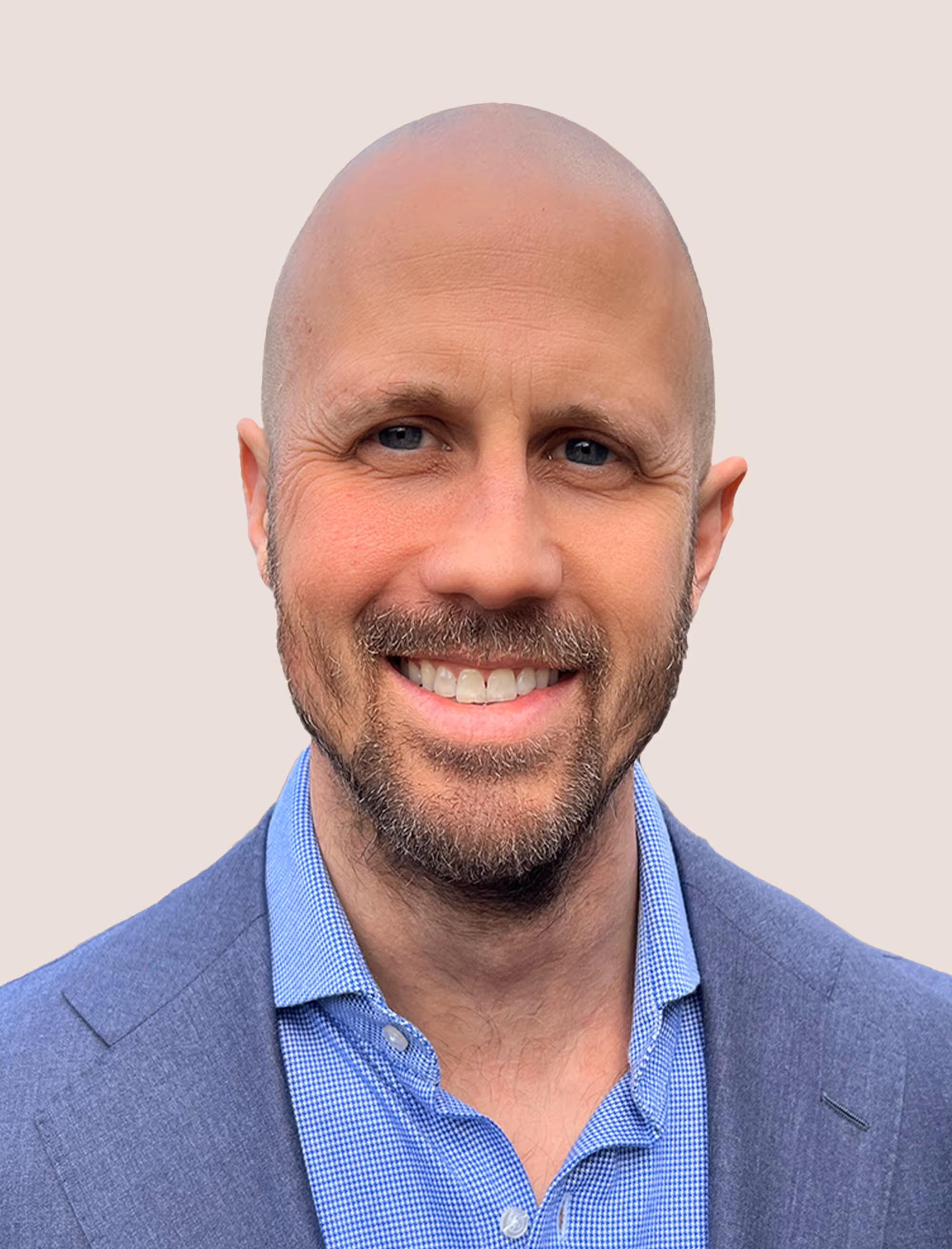 Smiling bald man with light beard wearing a blue blazer and checkered shirt on a plain light background.