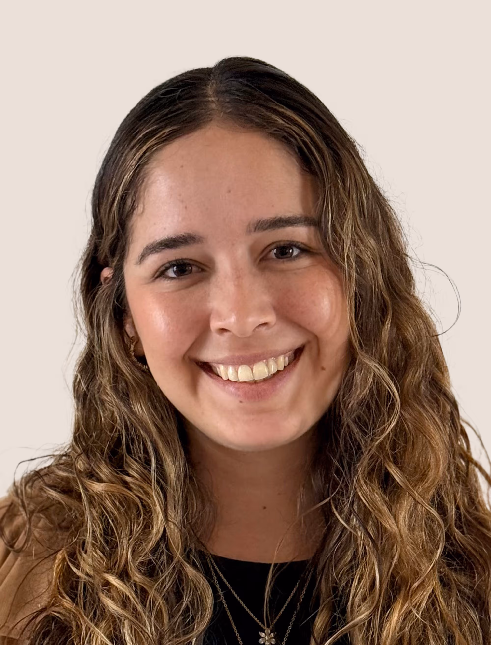 Young woman with long curly brown hair smiling against a plain light background.