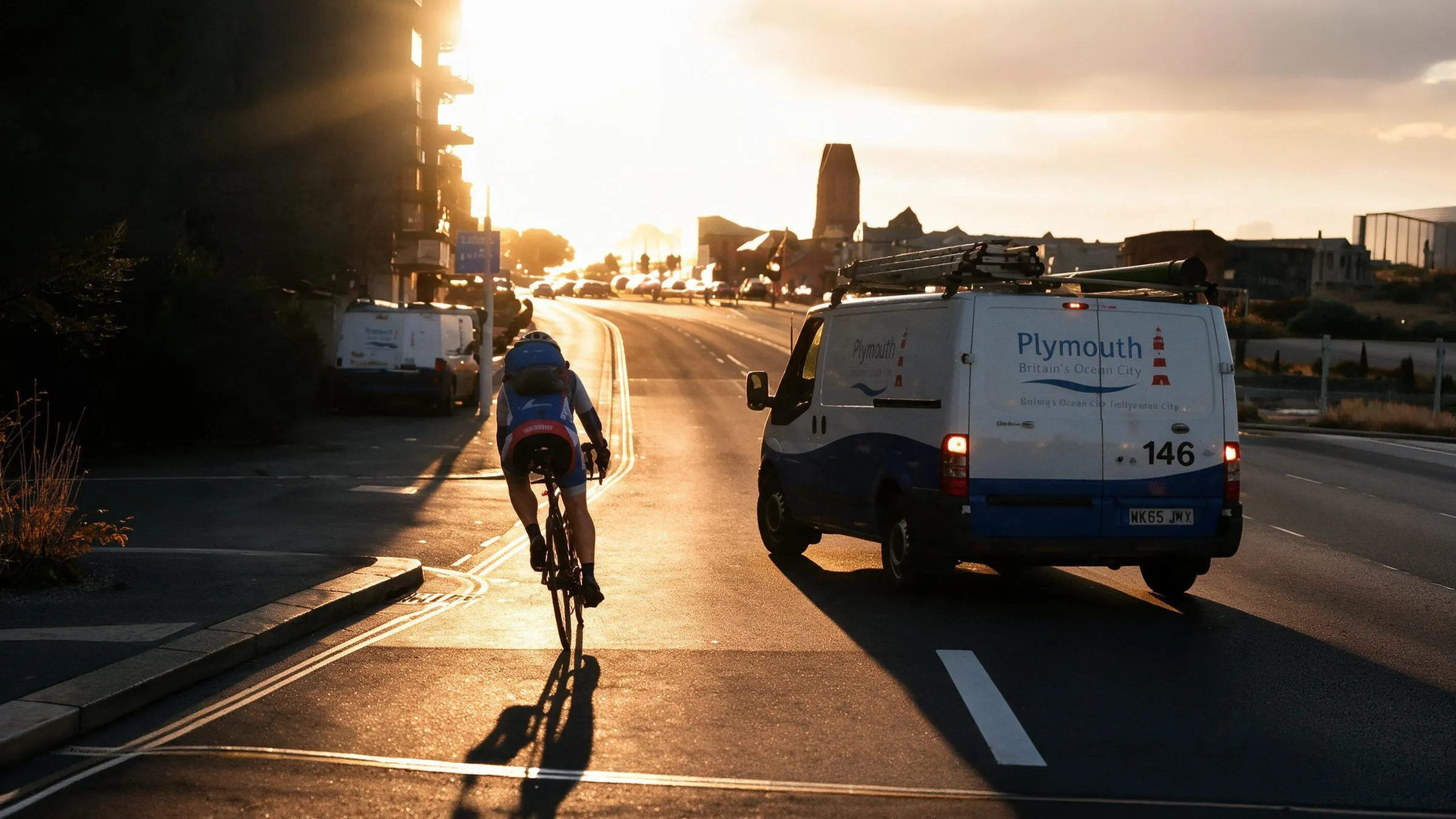 A cyclist riding beside a van on a narrow road in low sun
