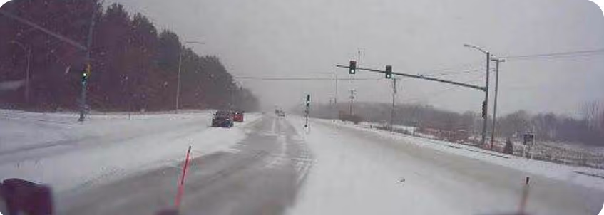 Snowplow dash cam view of a mostly snow-covered road with a small clear portion
